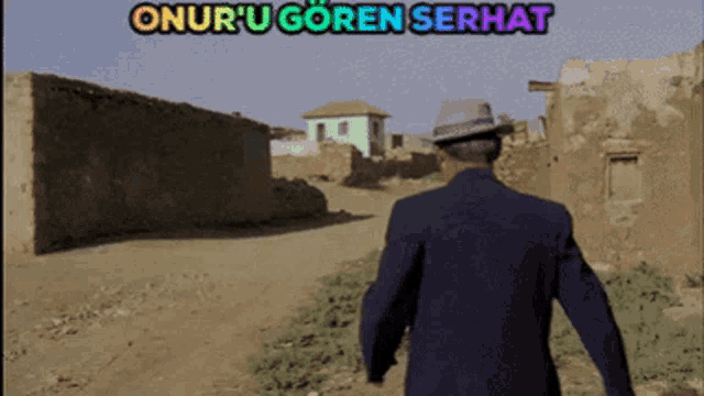 a man in a suit and hat is walking down a dirt road with onur u goren serhat above him