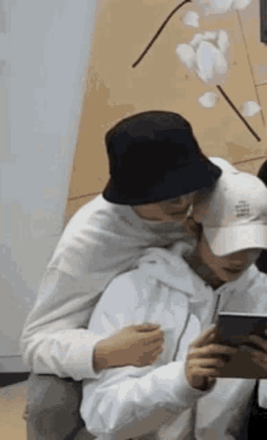 a man in a bucket hat is hugging another man in a white hoodie .