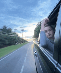 a man is sticking his head out of a car window while driving down a road