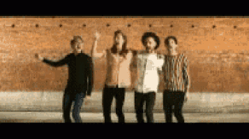 a group of four men are standing next to each other in front of a brick wall .