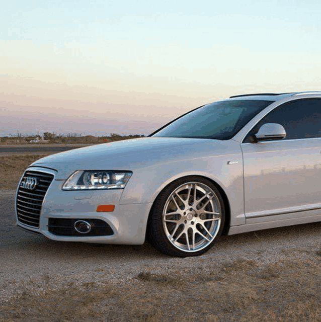 a white audi is parked on the side of a dirt road