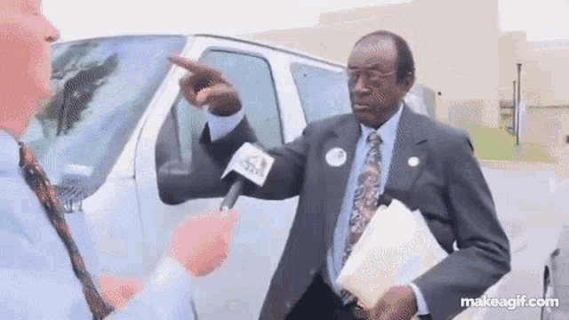 a man in a suit is pointing at another man in front of a white van .