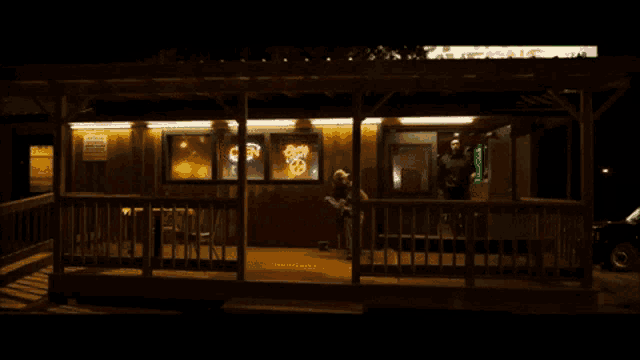 a man stands on a porch in front of a store with a neon sign that says open
