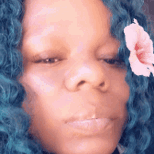 a close up of a woman 's face with blue hair and a pink flower in her hair .