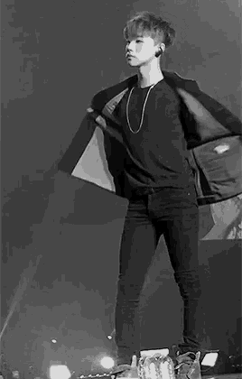 a black and white photo of a man standing on a stage with his hands on his hips .