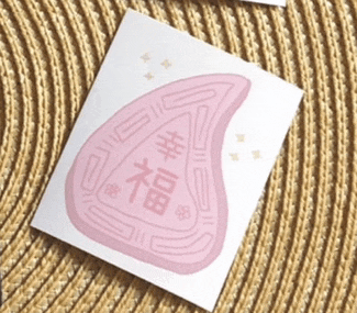 a pink sticker with chinese writing on it sits on a knitted surface