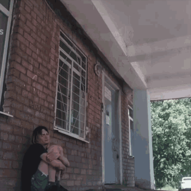 a woman sits in front of a brick building with a sign on the window that says ' s '