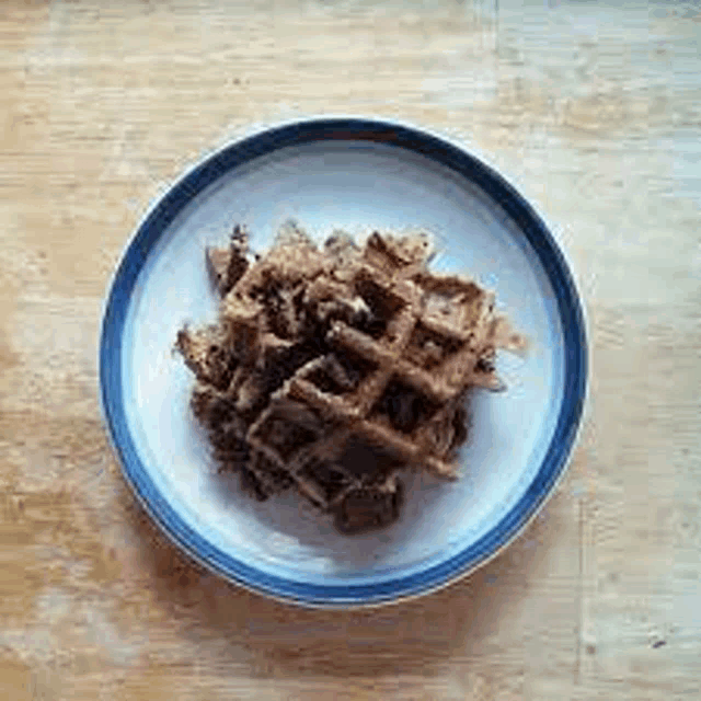 a white plate topped with a pile of chocolate waffles on a wooden table .