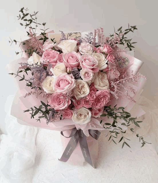 a bouquet of pink and white roses is wrapped in pink paper and tied with a ribbon