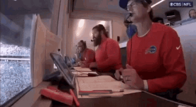 a group of men are sitting at a table in front of a window wearing red shirts with the word buffalo on them .