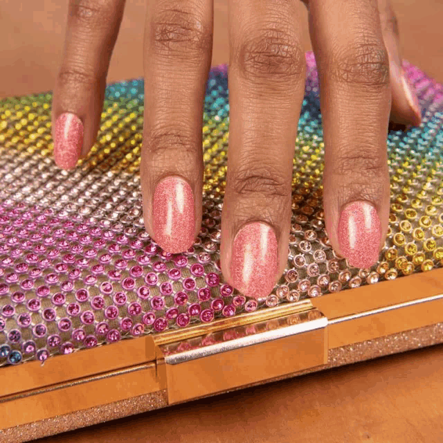 a woman 's nails are painted pink and she is holding a clutch bag