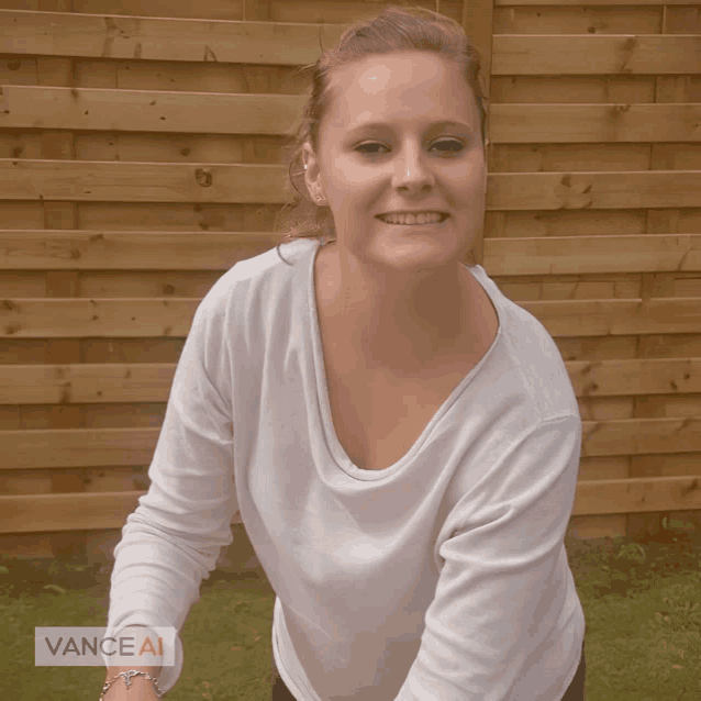 a woman in a white shirt is smiling in front of a wooden fence with vanceai written in the corner