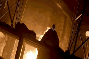 a man is standing in front of a fire in a dark room