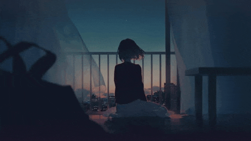 a girl is sitting on the floor on a balcony looking out at the city at night .