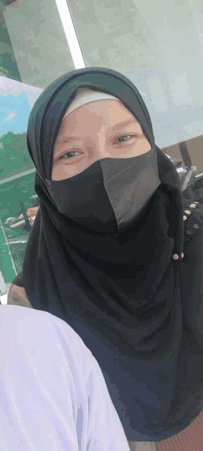 a woman wearing a black hijab and a black face mask smiles