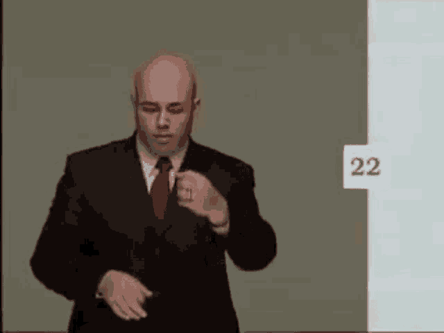 a bald man in a suit and tie is standing in front of a wall with the number 22 on it