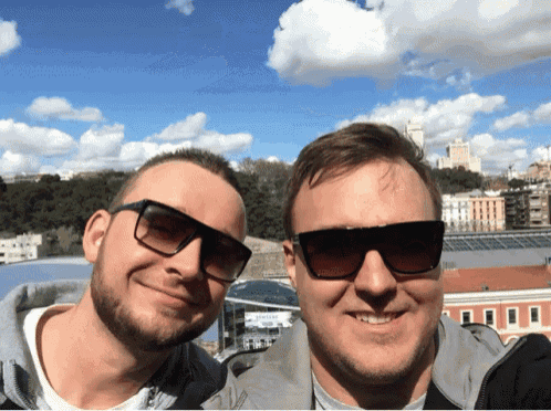 two men wearing sunglasses pose for a picture in front of a building that says ' samsung ' on it