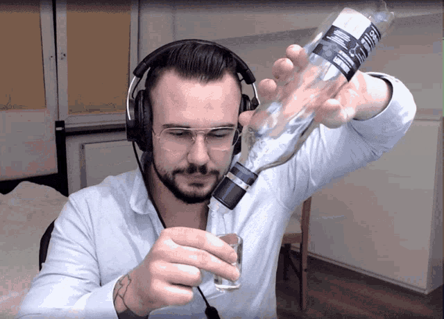 a man wearing headphones and glasses is pouring a shot of vodka from a bottle