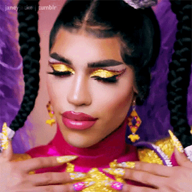 a close up of a drag queen 's face with purple and gold makeup and nails .