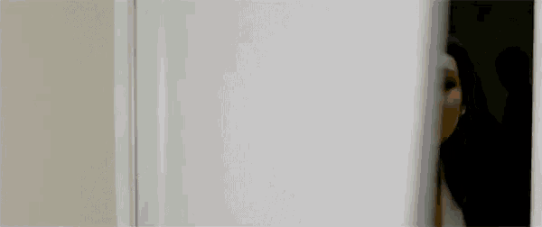 a woman is peeking out from behind a door in a dark room