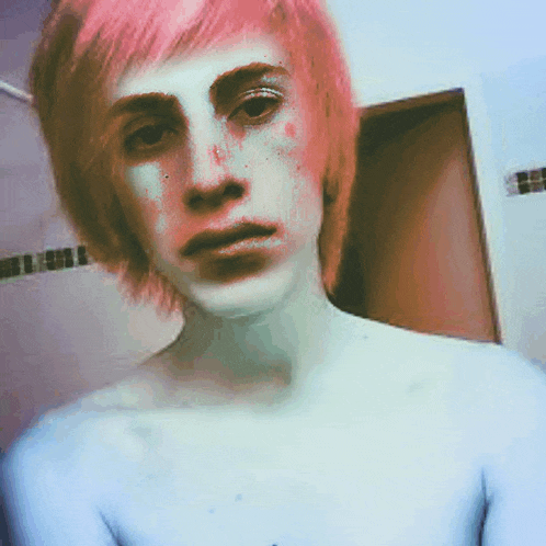 a shirtless man with pink hair looks at the camera in a bathroom