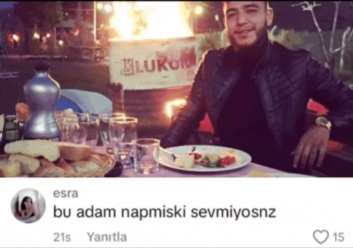 a man sits at a table with a plate of food in front of a sign that says ' kluku '