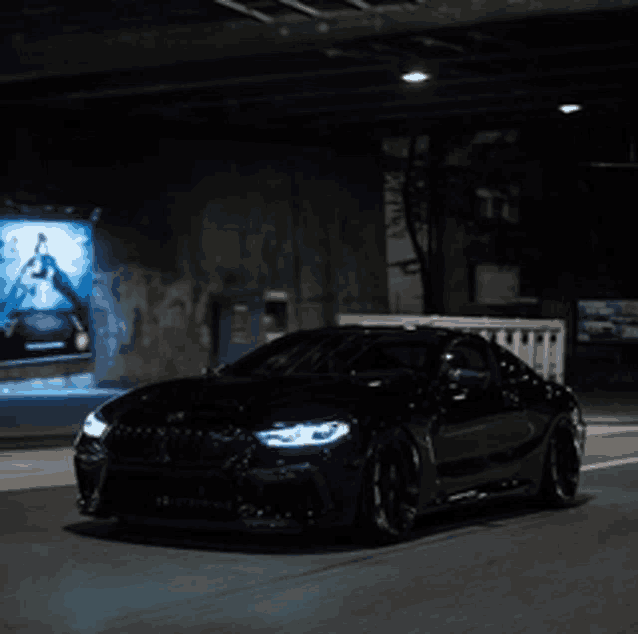 a black car is driving under a bridge with a billboard behind it