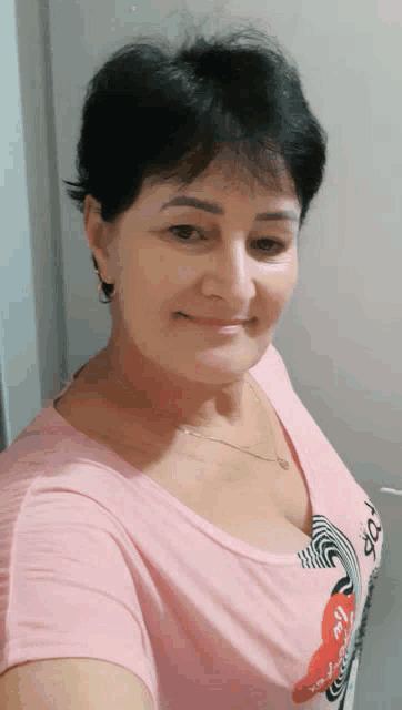 a woman in a pink shirt is taking a selfie and smiling .