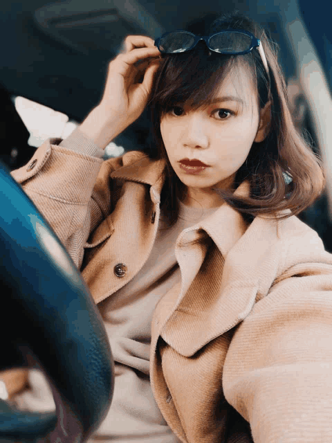 a woman wearing glasses and a tan coat is sitting in a car