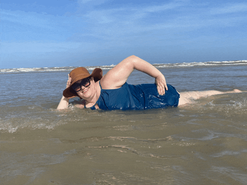 a woman in a hat and sunglasses is laying in the ocean