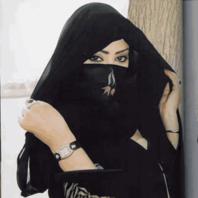 a woman wearing a black veil and a watch is standing in front of a tree .