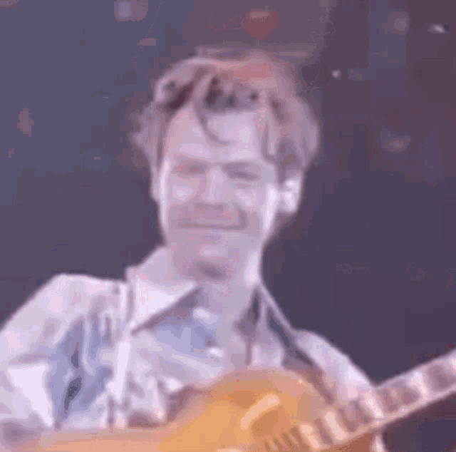 a man in a blue shirt is playing a guitar on a stage .