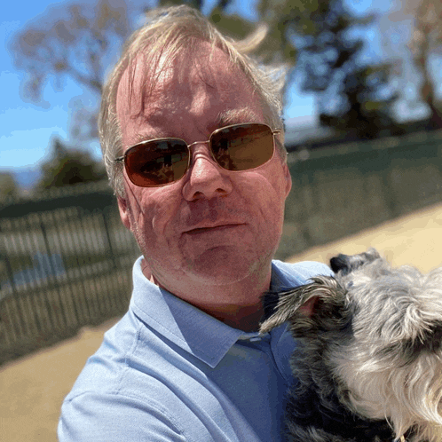 a man in sunglasses holds a small dog