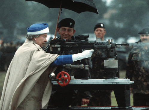 queen elizabeth ii looks at a machine gun with soldiers behind her