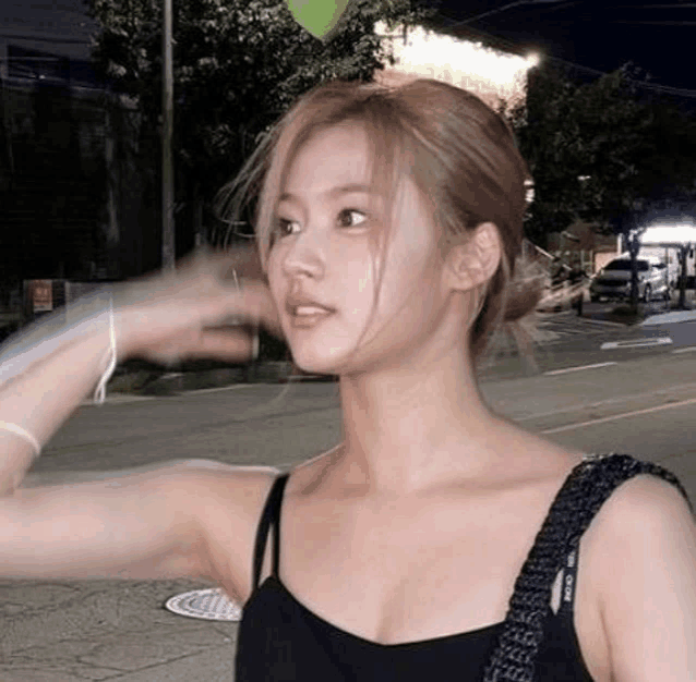 a woman in a black tank top is standing on a sidewalk in front of a building at night .