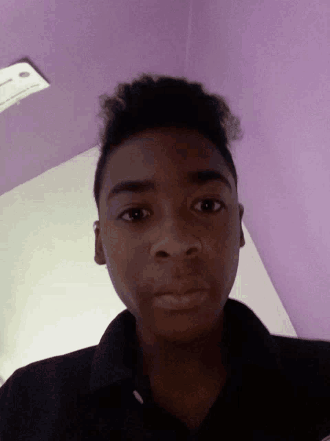 a young man in a black shirt looks at the camera with a purple wall in the background