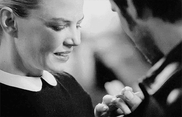 a man and a woman are holding hands and looking at each other in a black and white photo .