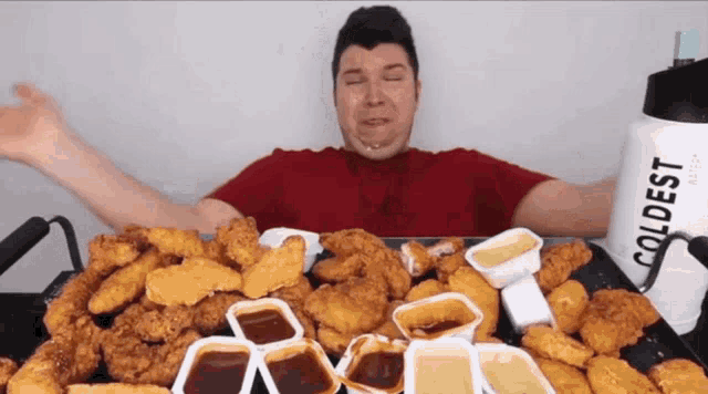 a man in a red shirt is eating chicken nuggets and dipping sauces next to a bottle of coldest water