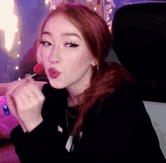 a girl with red hair is licking a lollipop in her mouth