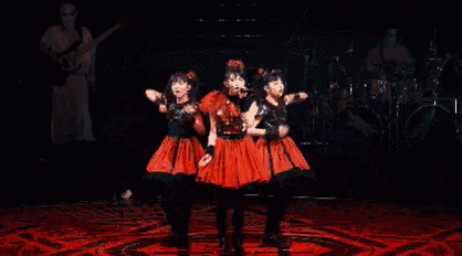 three women in red dresses are dancing on a stage in a dark room .