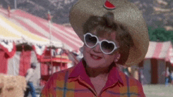 a woman wearing a hat and heart shaped sunglasses is standing in front of a circus tent .