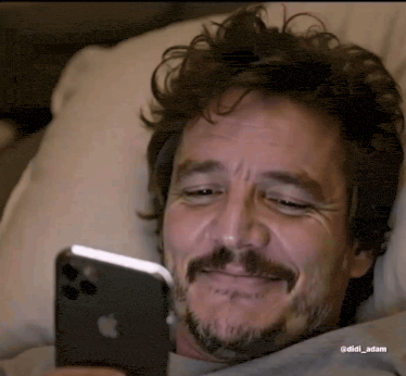 a man with a beard is laying in bed looking at his iphone .