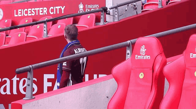 a man wearing a jersey that says alberts sits in a stadium with emirates seats