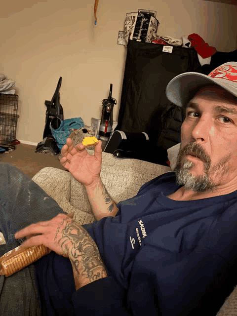 a man is sitting on a couch holding a piece of cheese and wearing a samsung shirt