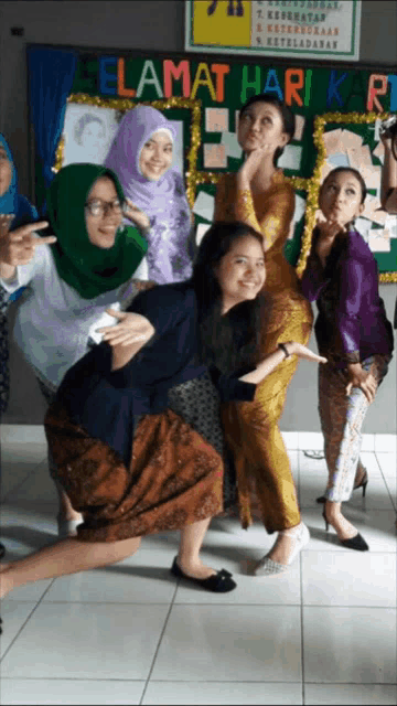 a group of women posing for a picture in front of a sign that says " selamat hari k "