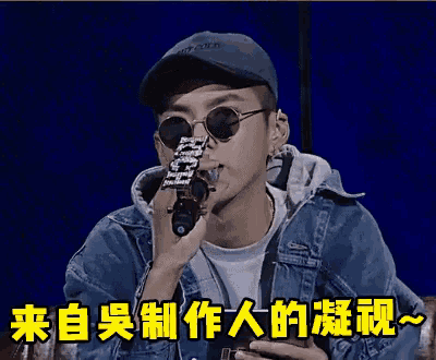 a man wearing sunglasses and a hat is holding a microphone with chinese writing behind him