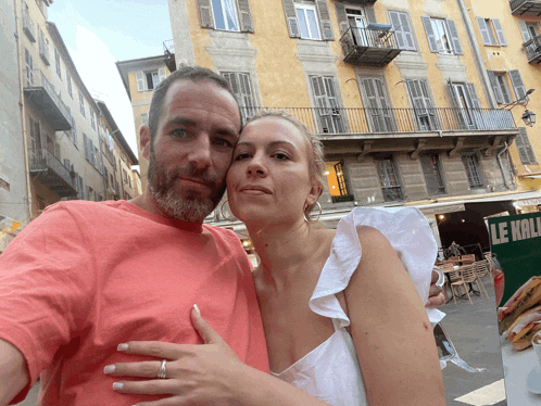 a man and a woman are posing for a picture in front of a sign that says " le kali "