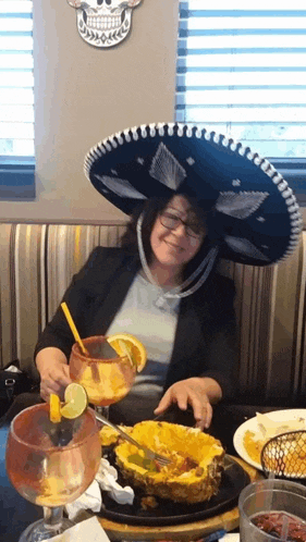 a woman wearing a sombrero sits at a table with a plate of food and drinks