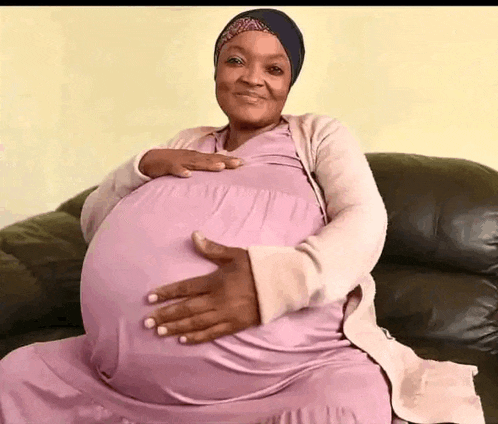 a pregnant woman is sitting on a couch holding her stomach .