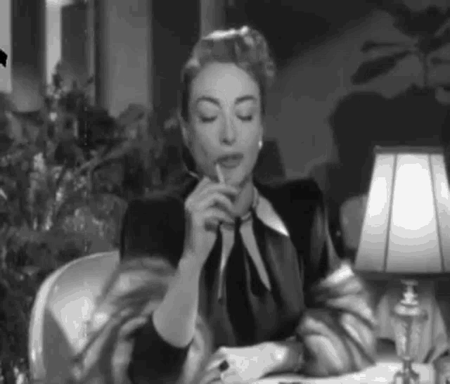 a woman is sitting at a table smoking a cigarette and drinking from a cup .